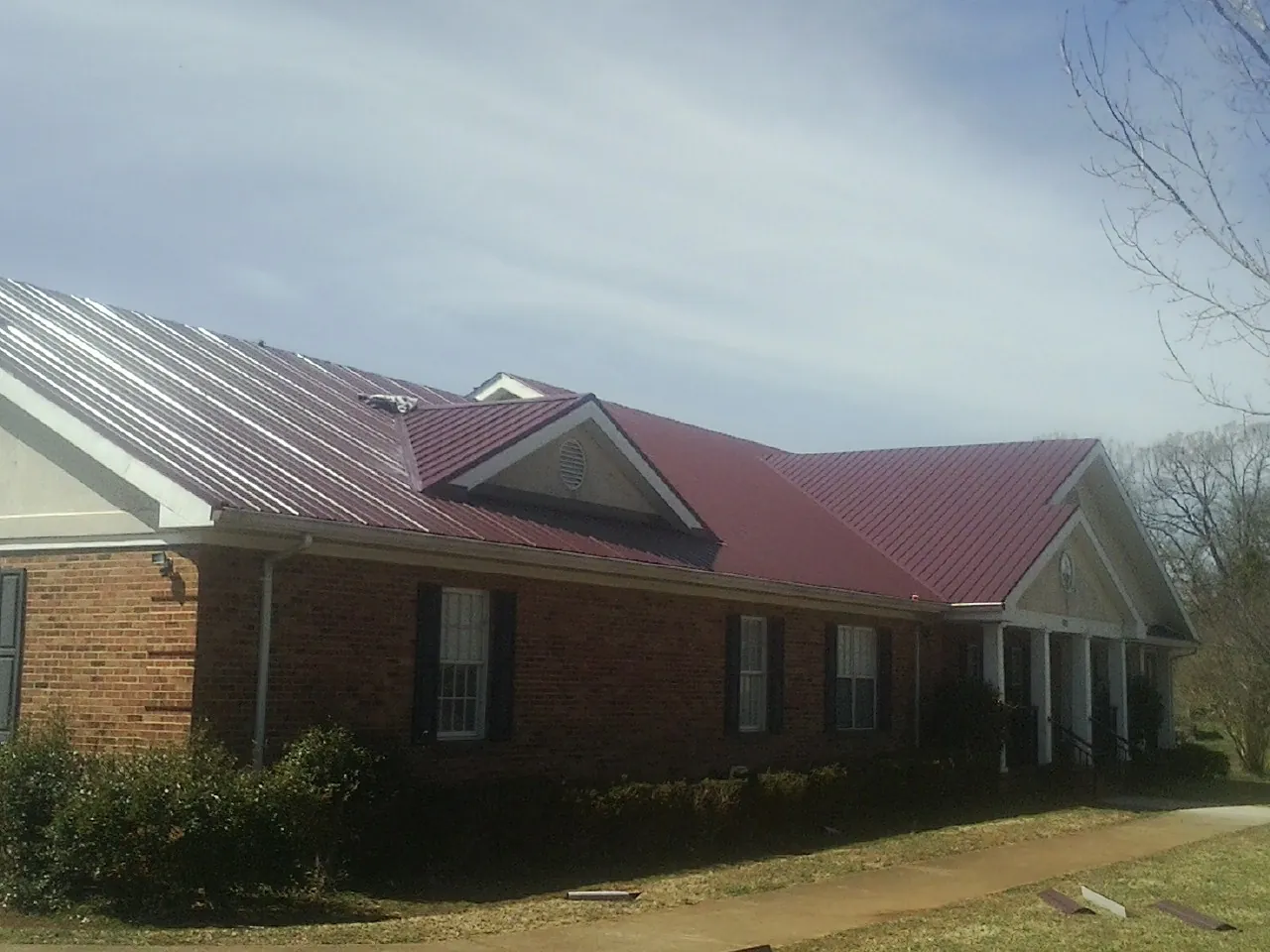 Red metal roof with gabled entries on a long brick building, from a Hail Damage Roof Repair job in Yankton