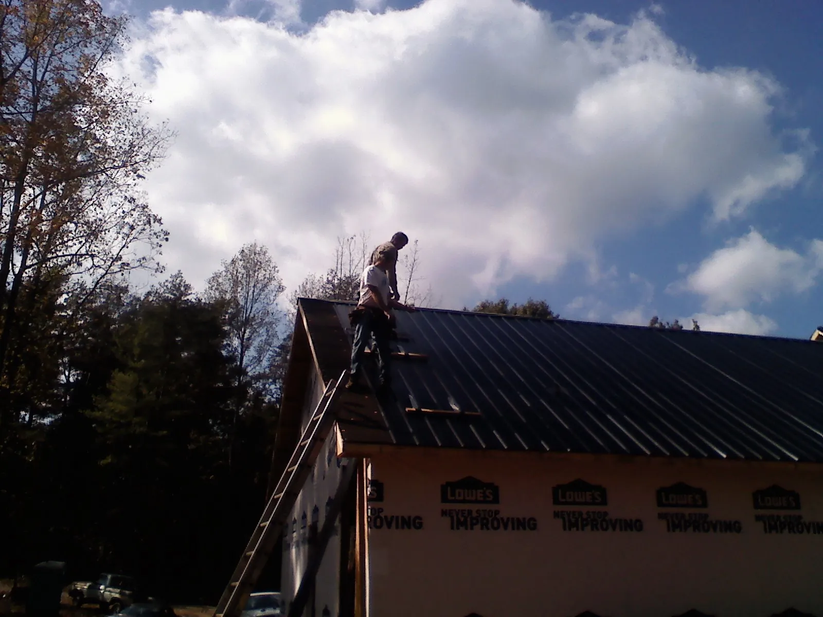 Roofer fastening dark metal panels high against a cloudy sky, from a Roof Inspection job in Yankton