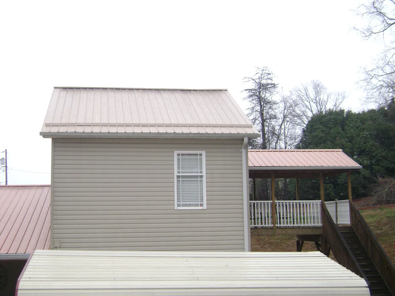 Tan metal roofs on a two story addition and attached porch, from a Roof Replacement job in Yankton